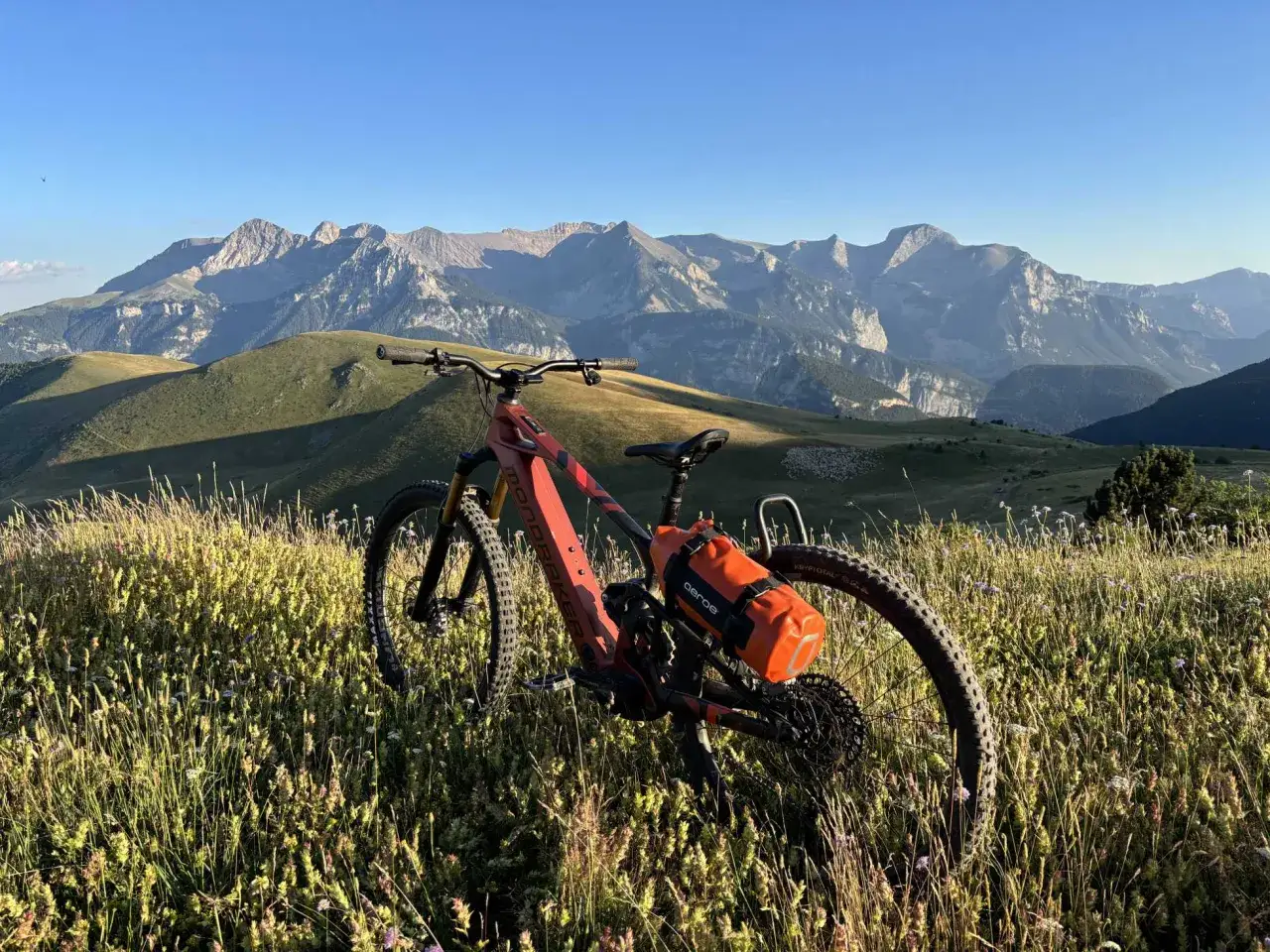 Bicicleta bikepacking lista para la aventura en un prado alpino con imponentes montañas al fondo.