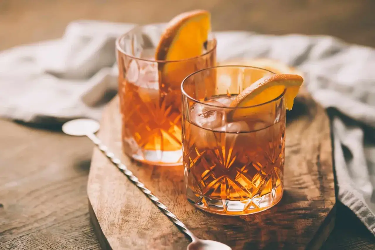 Dwa drinki: whisky z sokiem pomarańczowym, ozdobione plasterkami pomarańczy, na drewnianej desce.