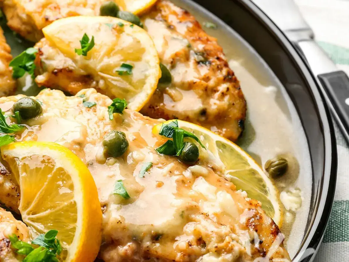 Delizioso pollo al limone con capperi e prezzemolo, servito in una salsa cremosa e guarnito con fette di limone.