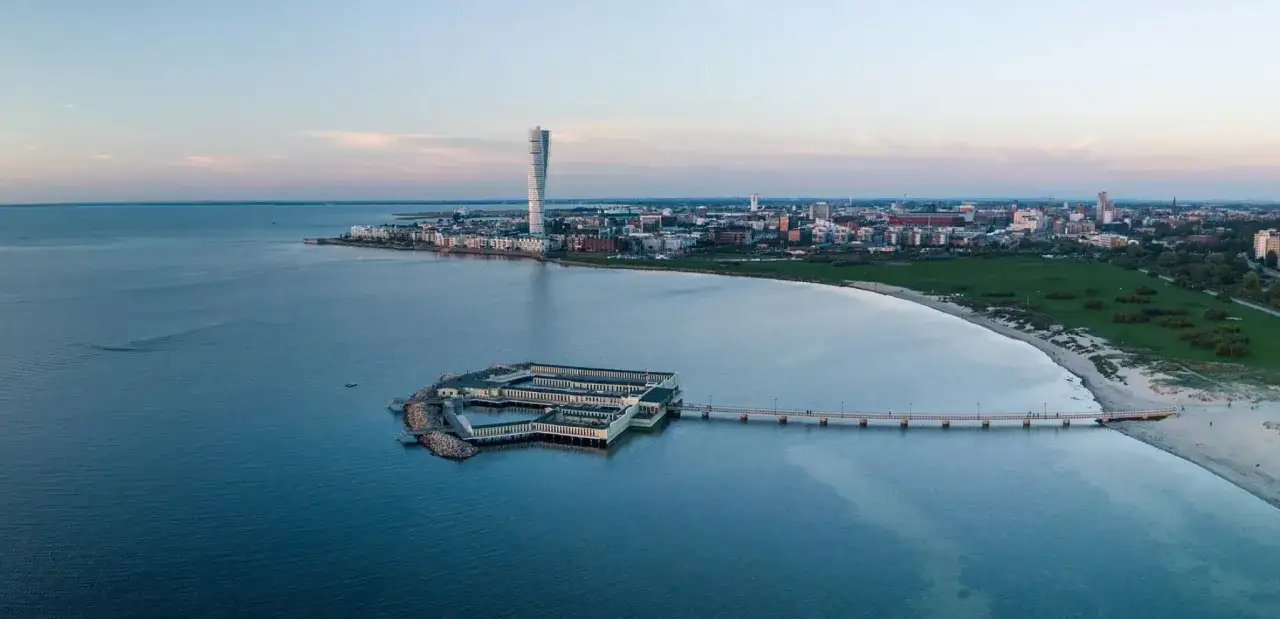 Malmös Turning Torso visning över havet, med Ribersborgs Kallbadhus och en strandpromenad.