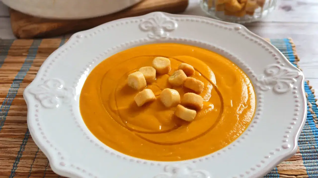 Un cremoso pure de calabaza al horno, servido en un plato blanco con croutons dorados.