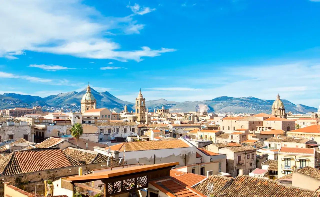 Palermo, marzec. Słoneczna pogoda nad miastem z kopułami i górami w tle.