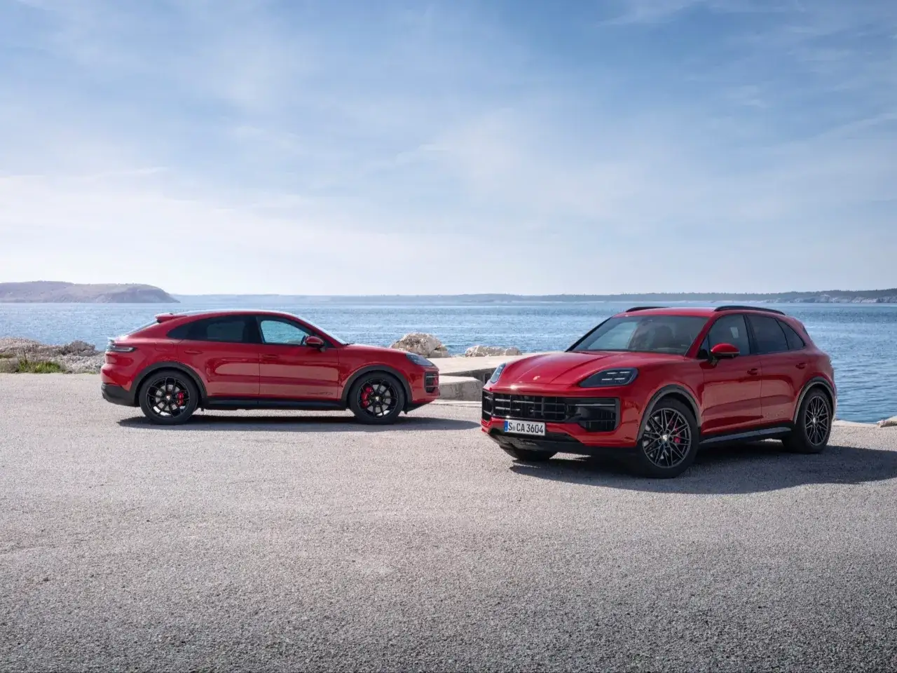 Dwa czerwone Porsche Cayenne GTS stoją przy morzu. Jeden to SUV, drugi to wersja coupe.