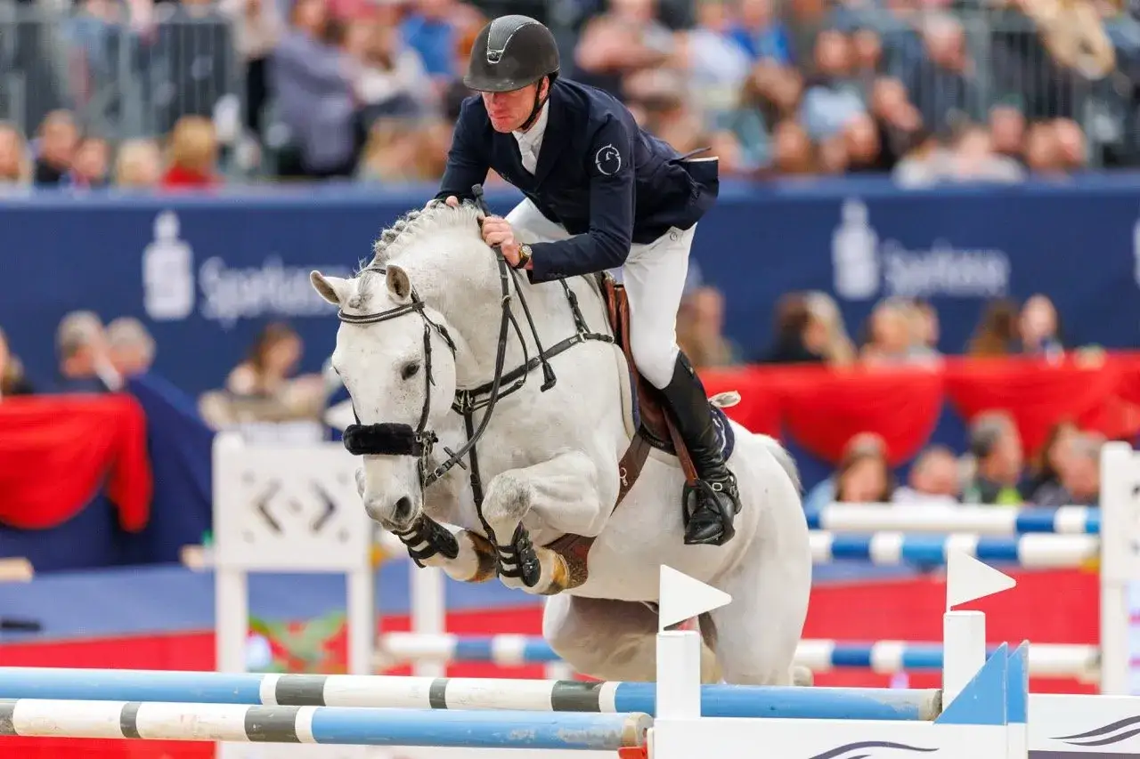 Un cavalier et son **kannan etalon** blanc franchissent un obstacle lors d'une compétition équestre.