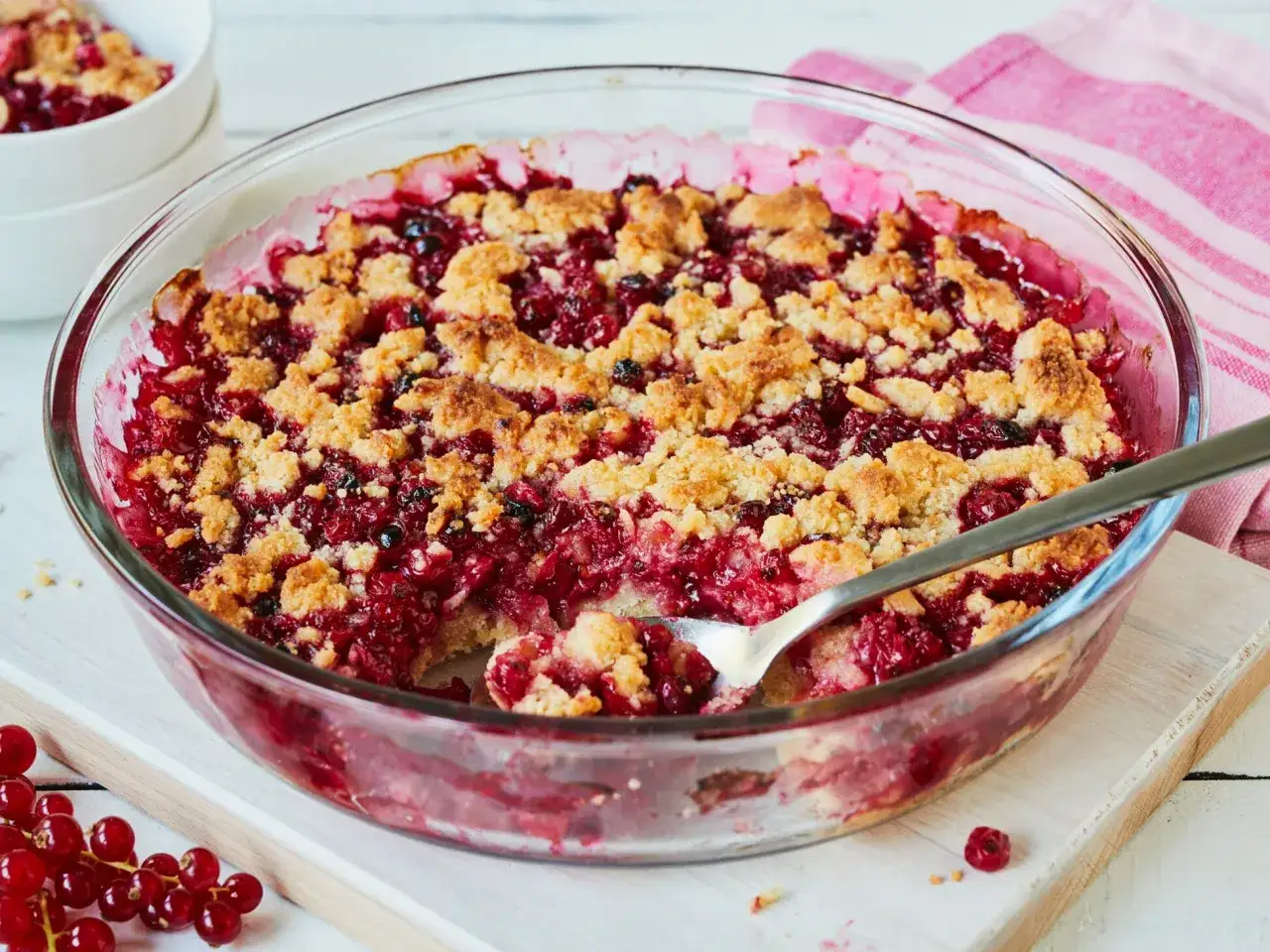 Ein leckerer Johannisbeer Crumble in einer Glasform, mit einer L&ouml;ffelportion herausgenommen.
