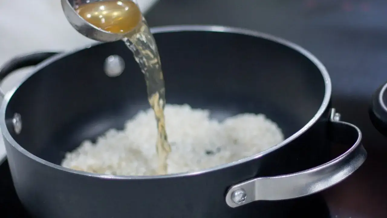 Brodo versato su riso originario in una pentola, inizio della cottura.