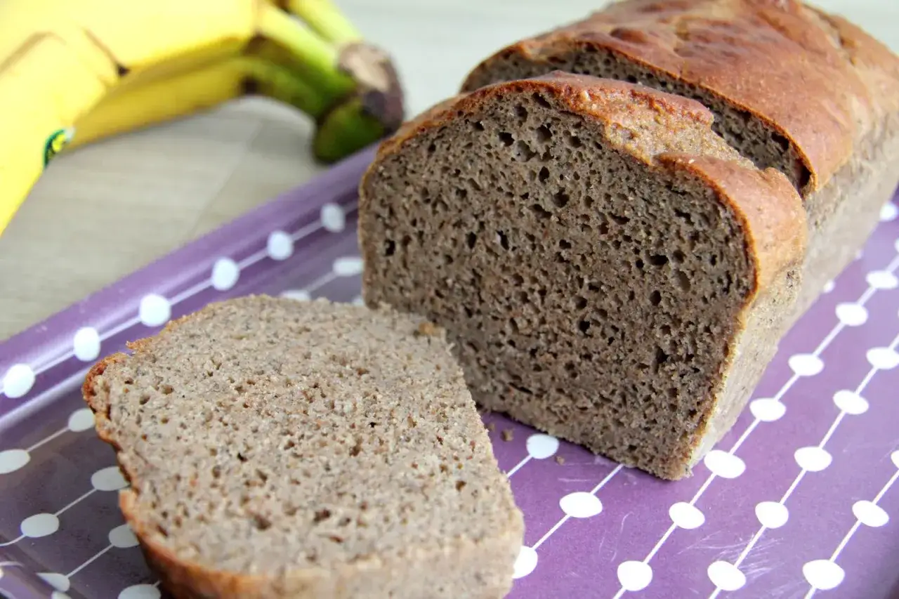 Pyszny, domowy proteinowy chlebek bananowy na fioletowej tacce z białymi kropkami. Obok leżą banany.