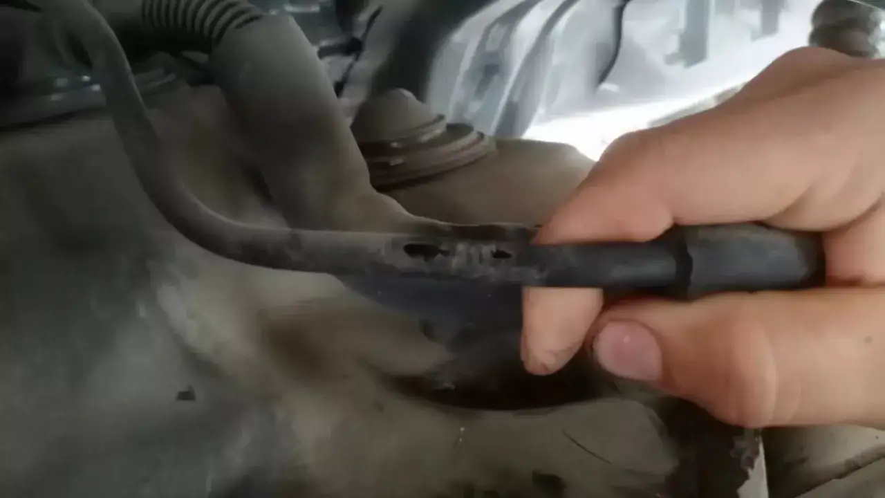 Main d'une personne inspectant un flexible de frein endommagé avec plusieurs perforations visibles.