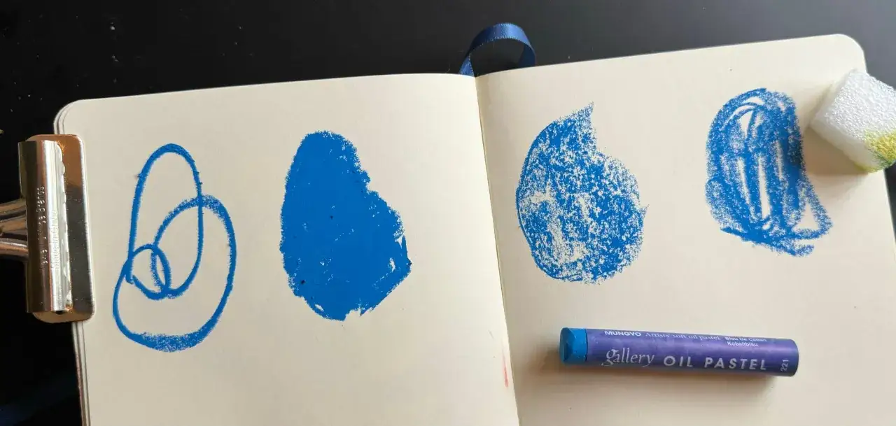 Próbki kolorów i techniki jak malować pastelami olejnymi. Niebieskie plamy i linie na papierze, obok kredka Mungyo.