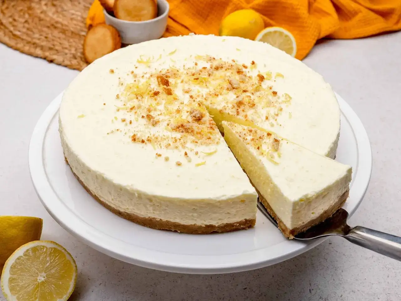 Cremige Philadelphia Torte mit Zitronennote, bestreut mit Kr&uuml;meln und Zitrusschale. Ein St&uuml;ck wird gerade serviert.