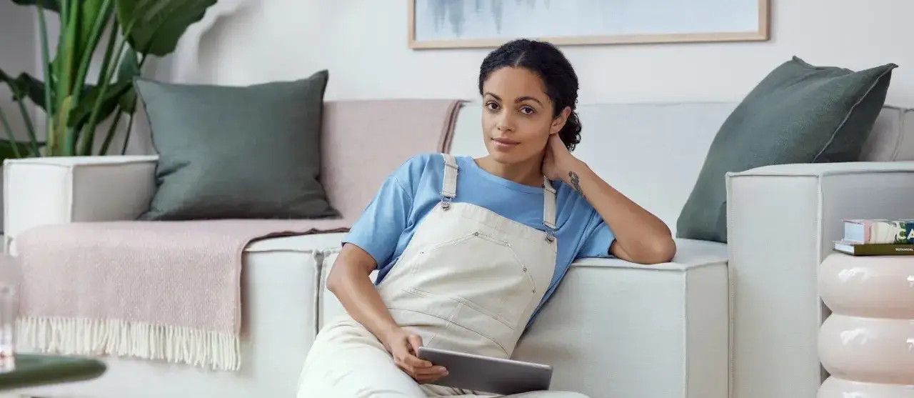 Vrouw overweegt wel of niet verhuizen test, zittend op de bank met tablet.