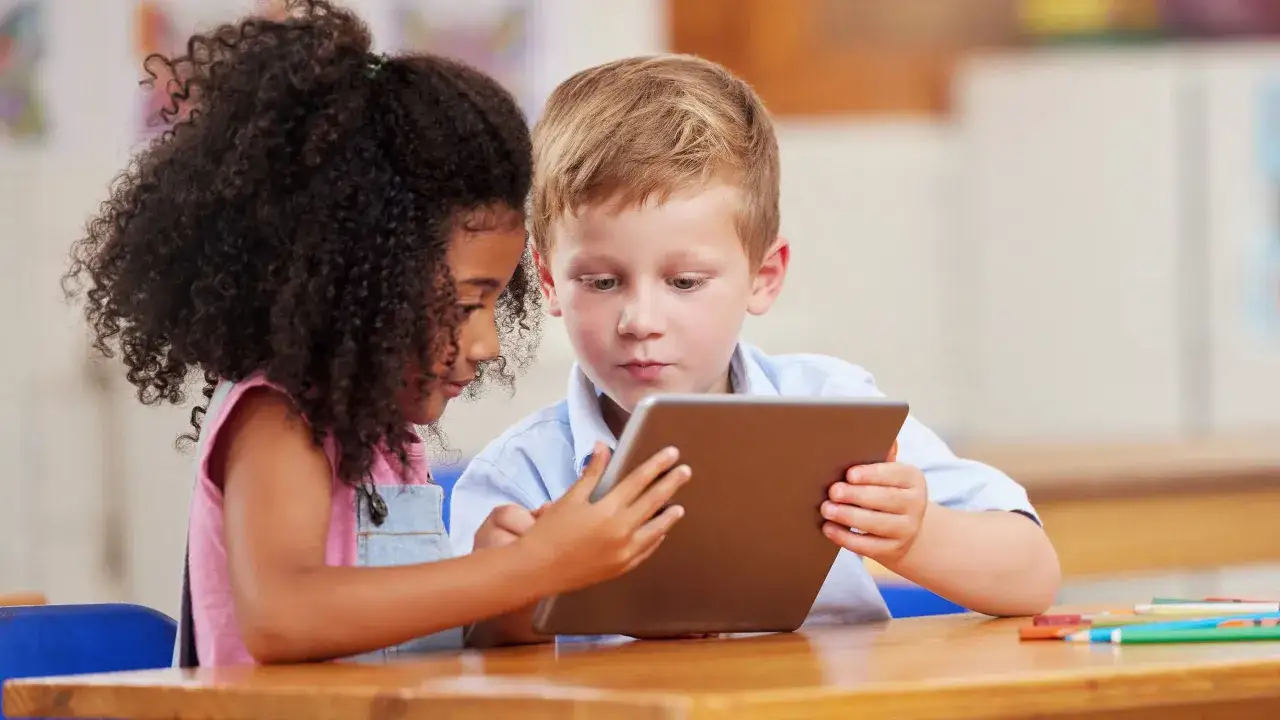 Zwei Kinder mit unterschiedlichem Hintergrund arbeiten gemeinsam an einem Tablet. Sie zeigen, wie kollaboratives Arbeiten im digitalen Zeitalter aussieht.