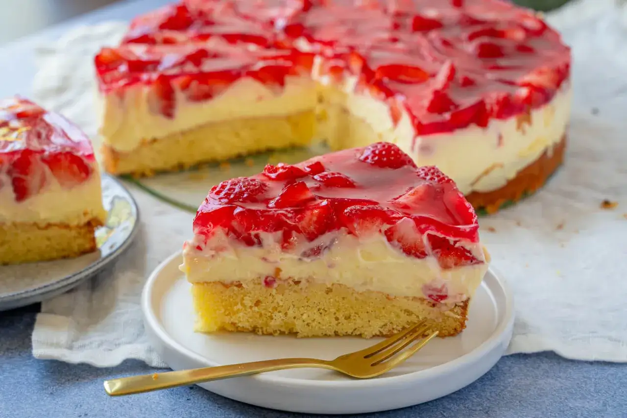 Ein saftiger Erdbeer Schmand Kuchen mit frischen Erdbeeren und gl&auml;nzender Tortenguss-Schicht. Ein St&uuml;ck auf einem Teller mit Gabel.