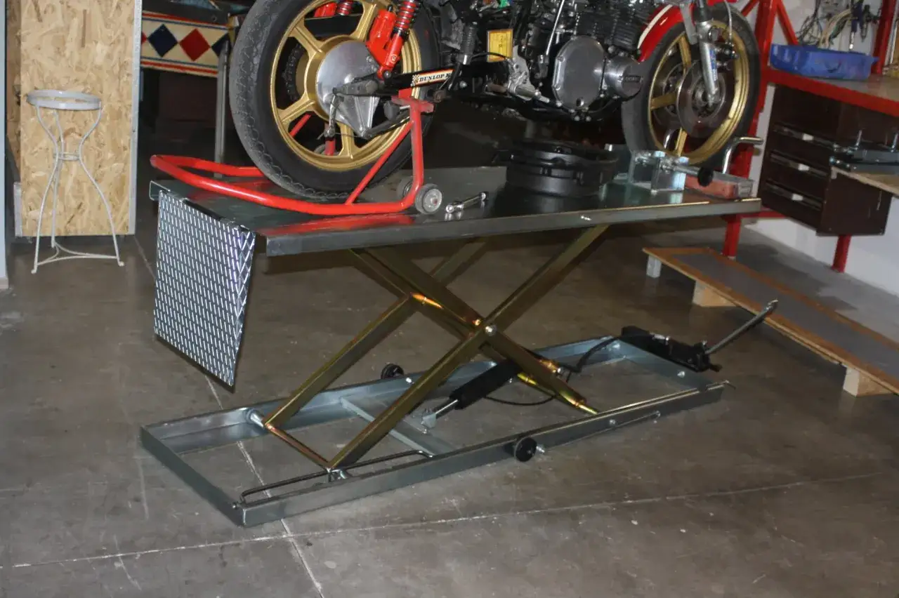 Moto su sollevatore a forbice in un garage officina fai da te. Attrezzi e parti di ricambio visibili.