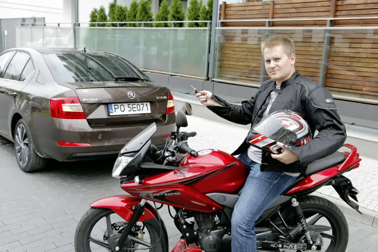 Kupiłem motocykl, co dalej? Czas na jazdę! Mężczyzna w kurtce motocyklowej z kaskiem w ręku siedzi na czerwonym motocyklu.