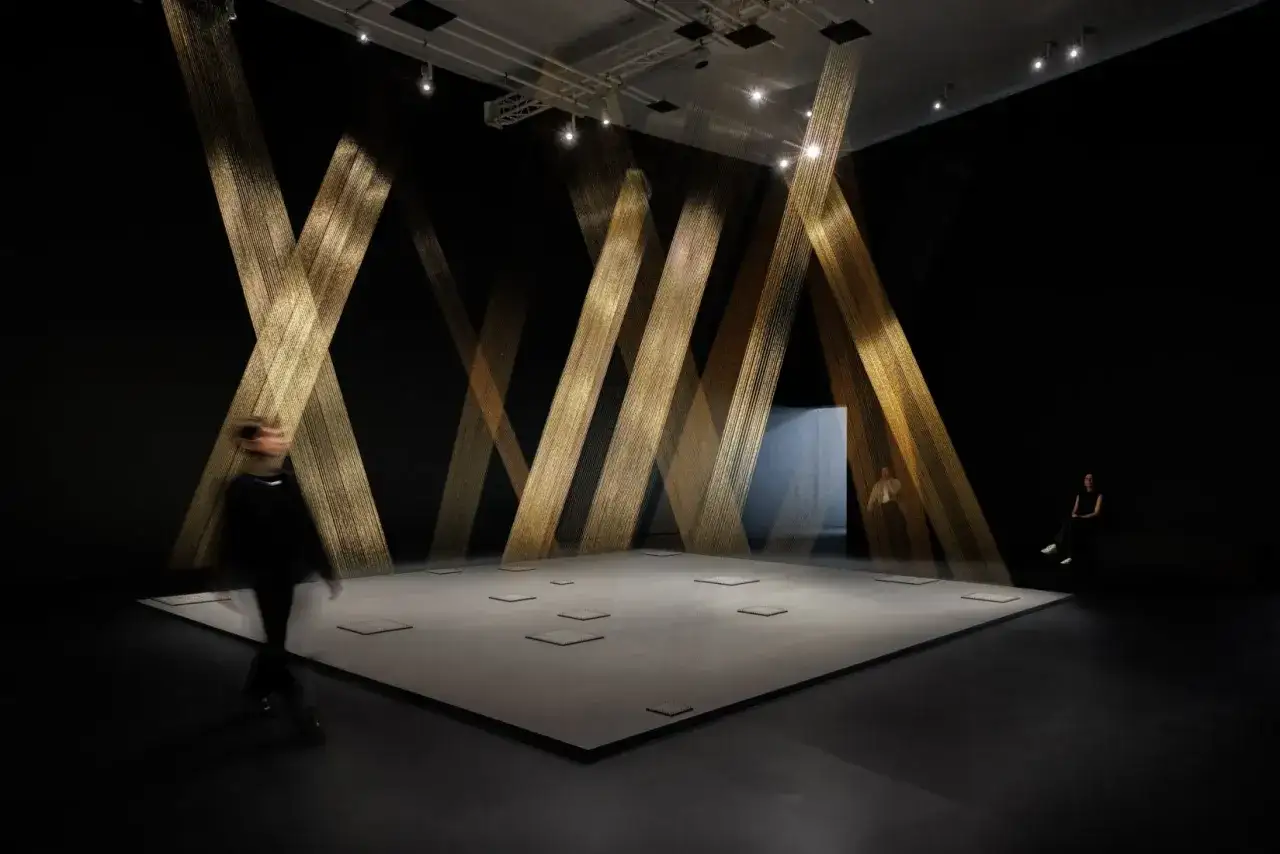 An immersive art installation, possibly part of François-Henri Pinault's collection, features golden strands cascading from the ceiling, creating a dramatic, ethereal space.