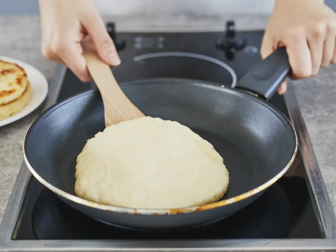 Ein Pfannenbrot-Rezept wird hier gezeigt: Teig wird in einer Pfanne mit einem Holzspatel geformt.