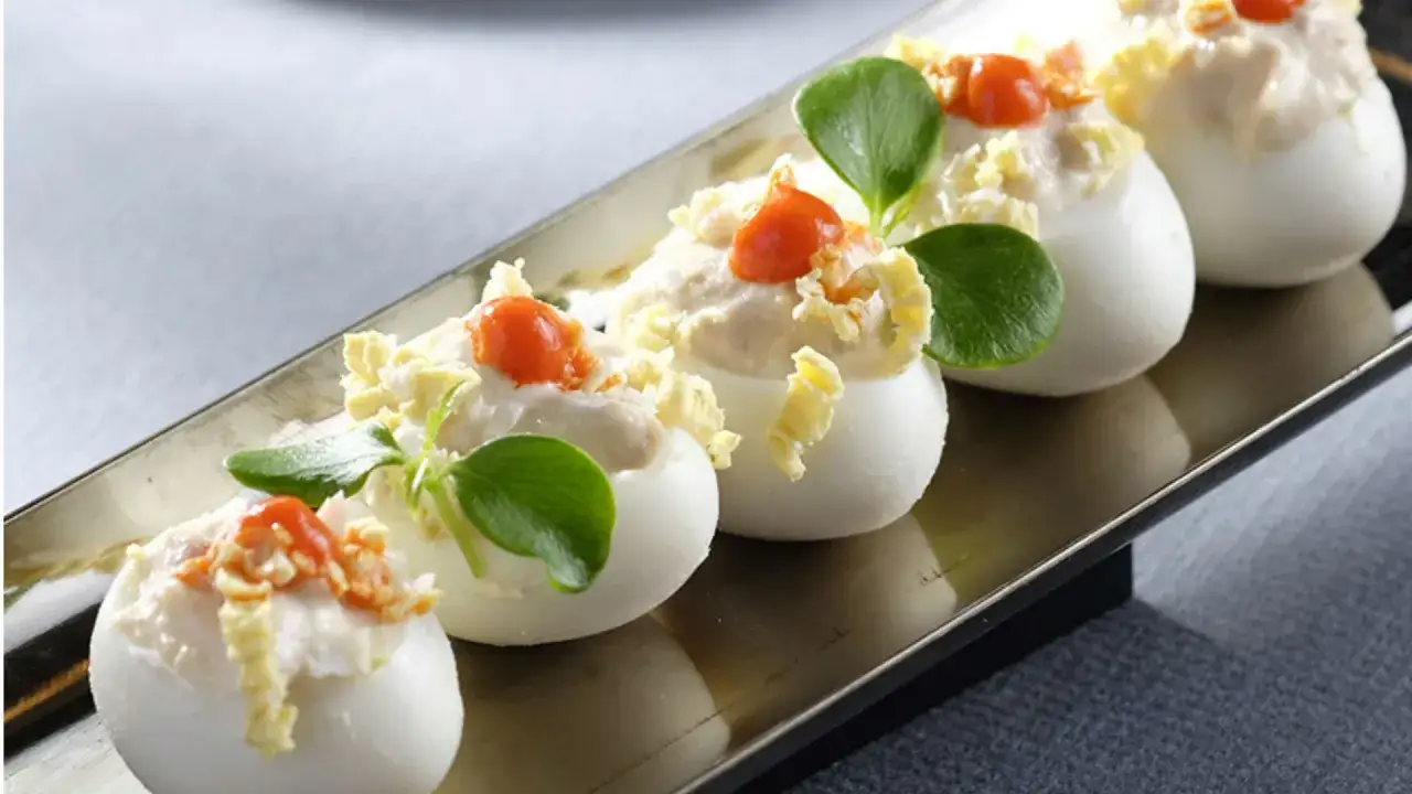 Deliciosos canapés con huevo de codorniz, rellenos de crema y decorados con un toque de pimentón y hojas verdes.