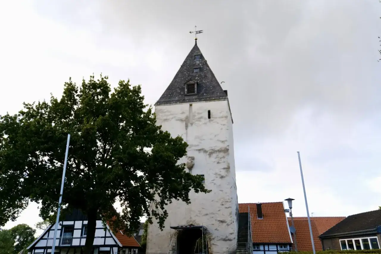 Der Stromberg in Oelde, ein alter Turm, ragt neben einem Baum und Fachwerkhäusern in den Himmel.