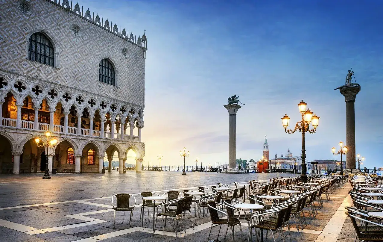 Piazza San Marco o wschodzie słońca. Pałac Dożów, kolumny z lwami i statuami, puste stoliki kawiarniane czekają na gości.