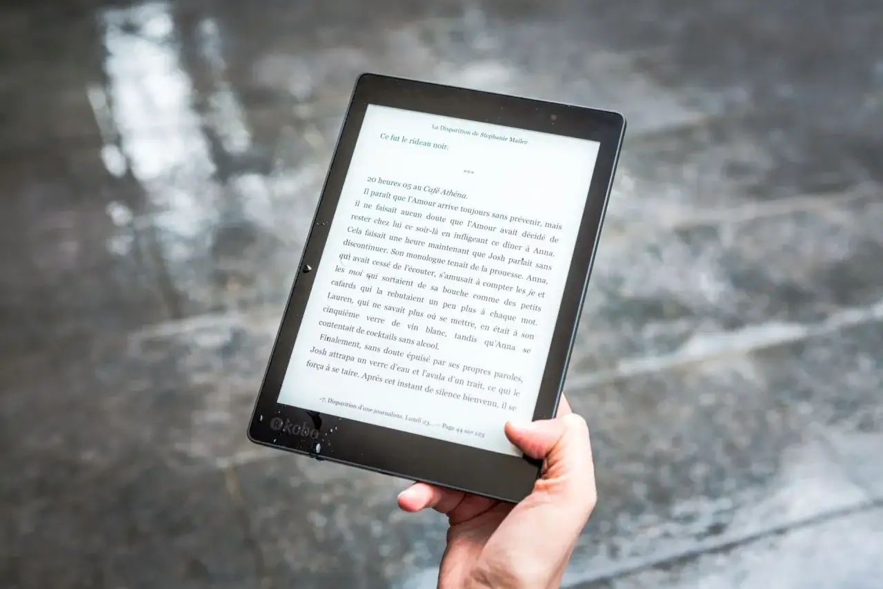 Dłoń trzyma czytnik ebook&oacute;w, na ekranie widać fragment książki. To świetny spos&oacute;b, by dowiedzieć się, ebook co to jest i jak wygodnie czytać.