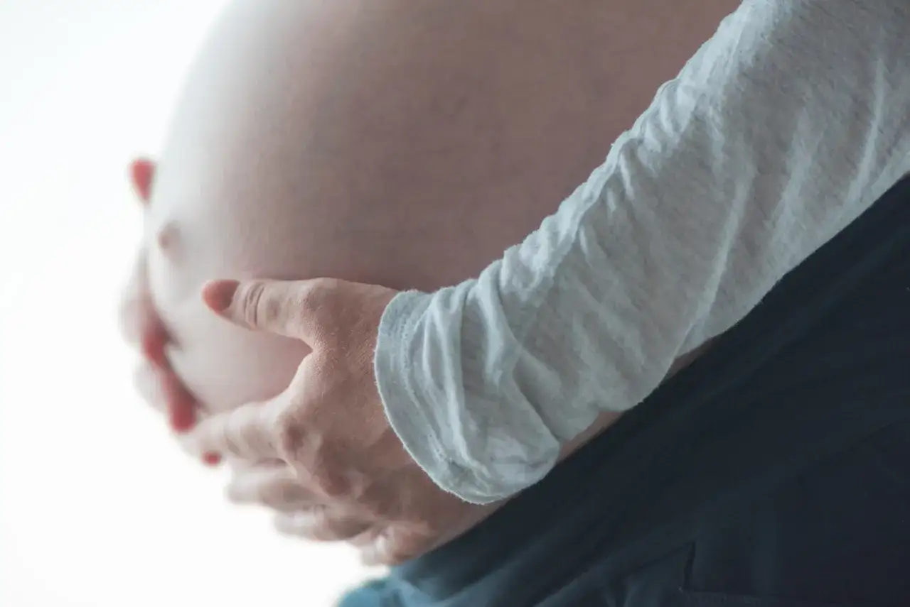 Dłoń obejmuje ciążowy brzuch. Częste oddawanie moczu w ciąży to normalny objaw.