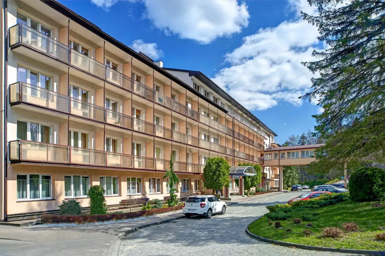 Sanatorium Górnik w Iwoniczu Zdroju, wielopiętrowy budynek z balkonami, otoczony zielenią, pod błękitnym niebem.