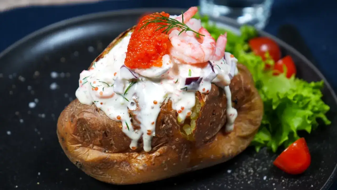 En perfekt bakad potatis i airfryer, toppad med en kr&auml;mig r&ouml;ra av r&auml;kor, rom och dill. Serveras med sallad och tomater.
