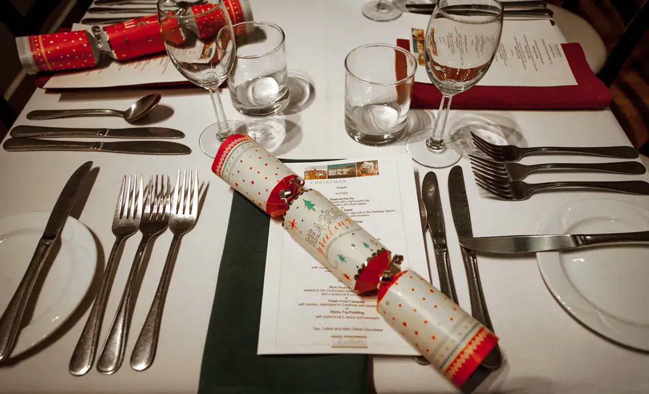 Tavola apparecchiata per le feste, con posate, bicchieri e un cracker natalizio. Chissà a chi si versa prima il vino per iniziare questo magico pranzo!