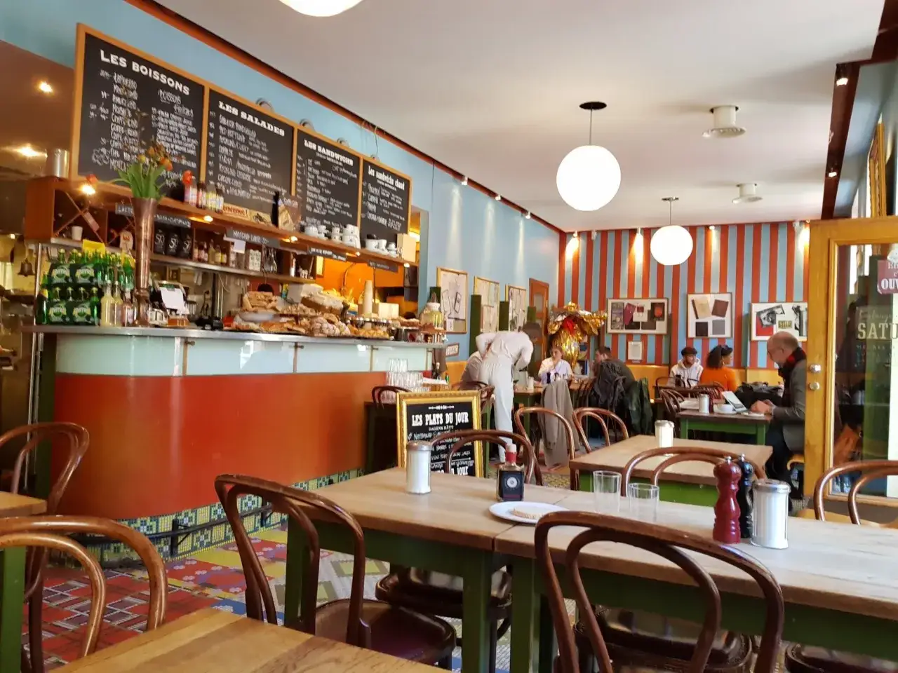 Mysig frukost i Stockholm. En livlig bistro med menyer på svarta tavlor, bakverk och sittande gäster.