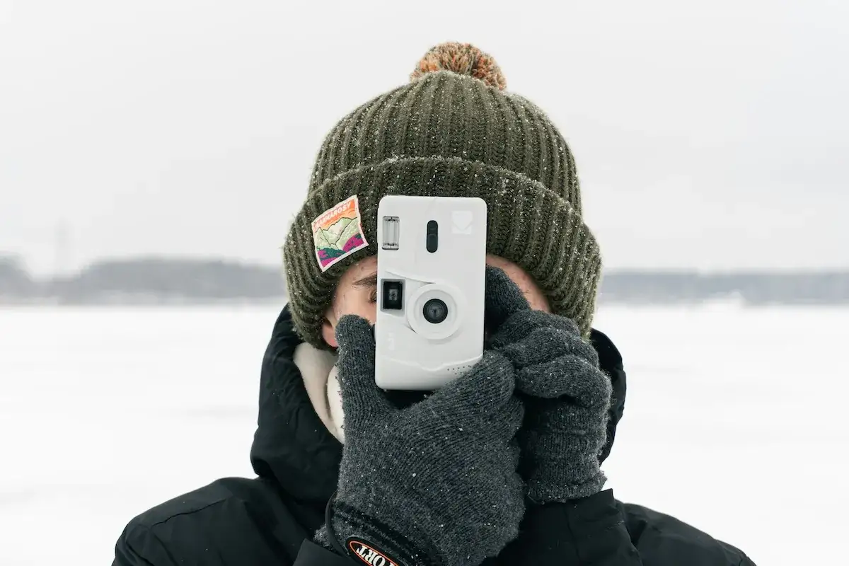 Osoba w zimowej czapce i rękawiczkach robi zdjęcie białym aparatem. To jej wyzwanie fotograficzne w mroźny dzień.