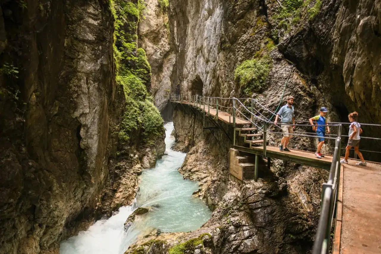 Familie wandert auf Stegen durch die Leutascher Geisterklamm, vorbei an tosendem Wasser und steilen Felsw&auml;nden.