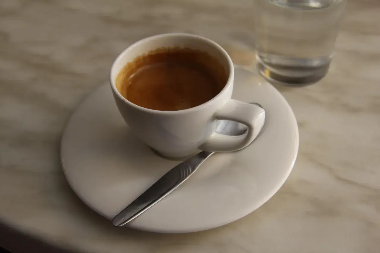 Elegancka filiżanka kawy espresso na talerzyku z łyżeczką i szklanką wody. Idealny spos&oacute;b, jak podawać kawę gościom, by poczuli się wyjątkowo.