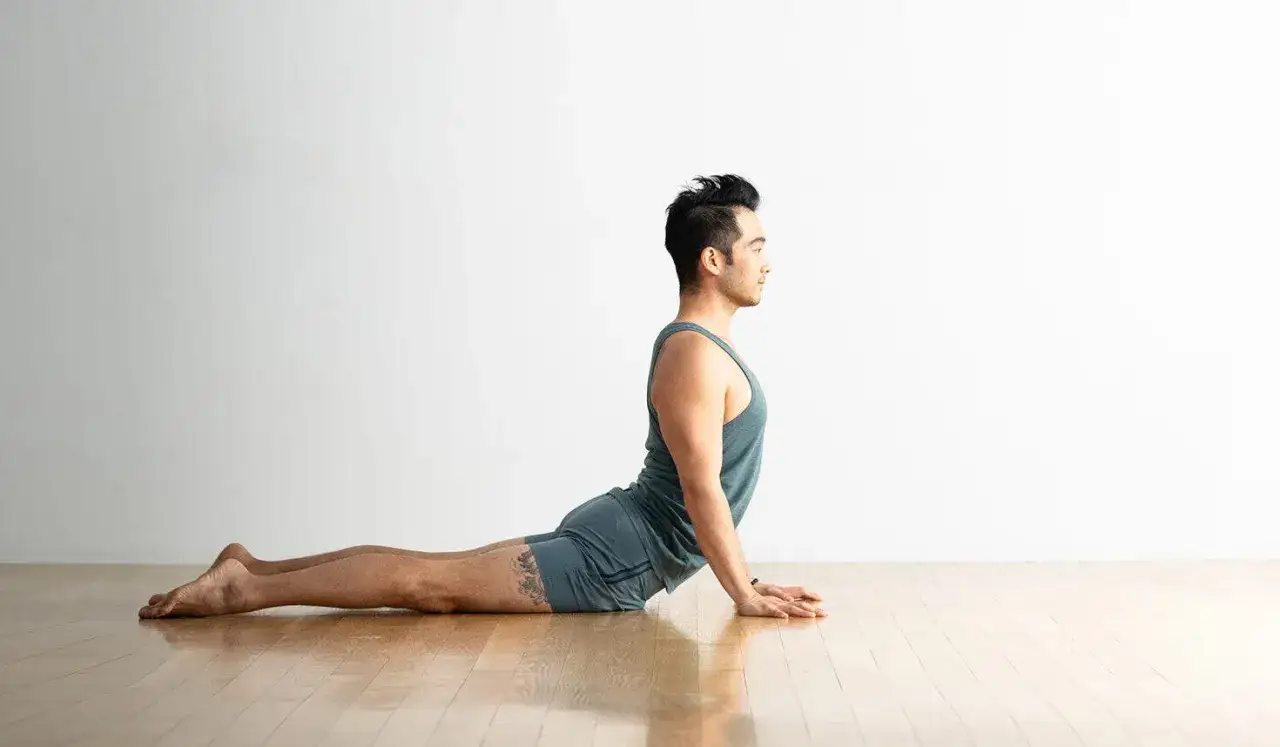 Mężczyzna w pozycji bhujangasana, z uniesionym tułowiem i wygiętym kręgosłupem, na drewnianej podłodze.