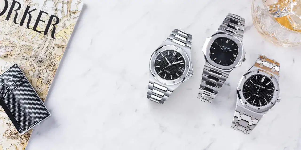 Orologi di lusso, tra cui un Patek Philippe Nautilus, che evocano lo stile di Gérald Genta. Accanto, un accendino e una rivista.