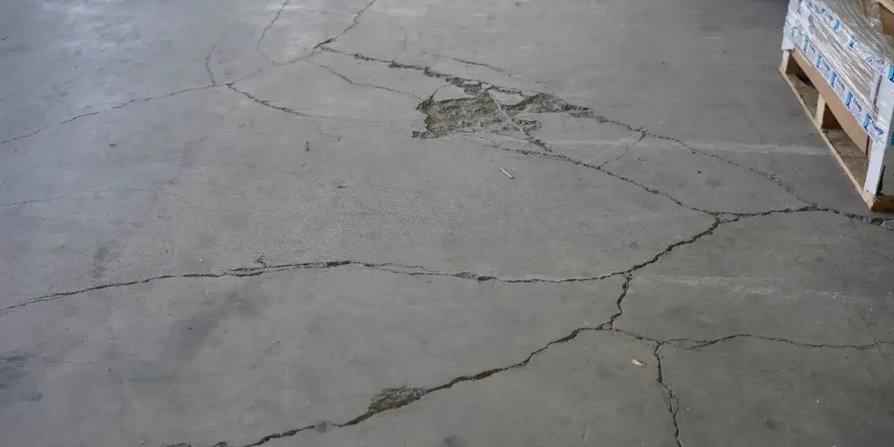 Suelo de hormig&oacute;n agrietado, mostrando la necesidad de aprender como hacer hormig&oacute;n para suelo resistente y duradero.
