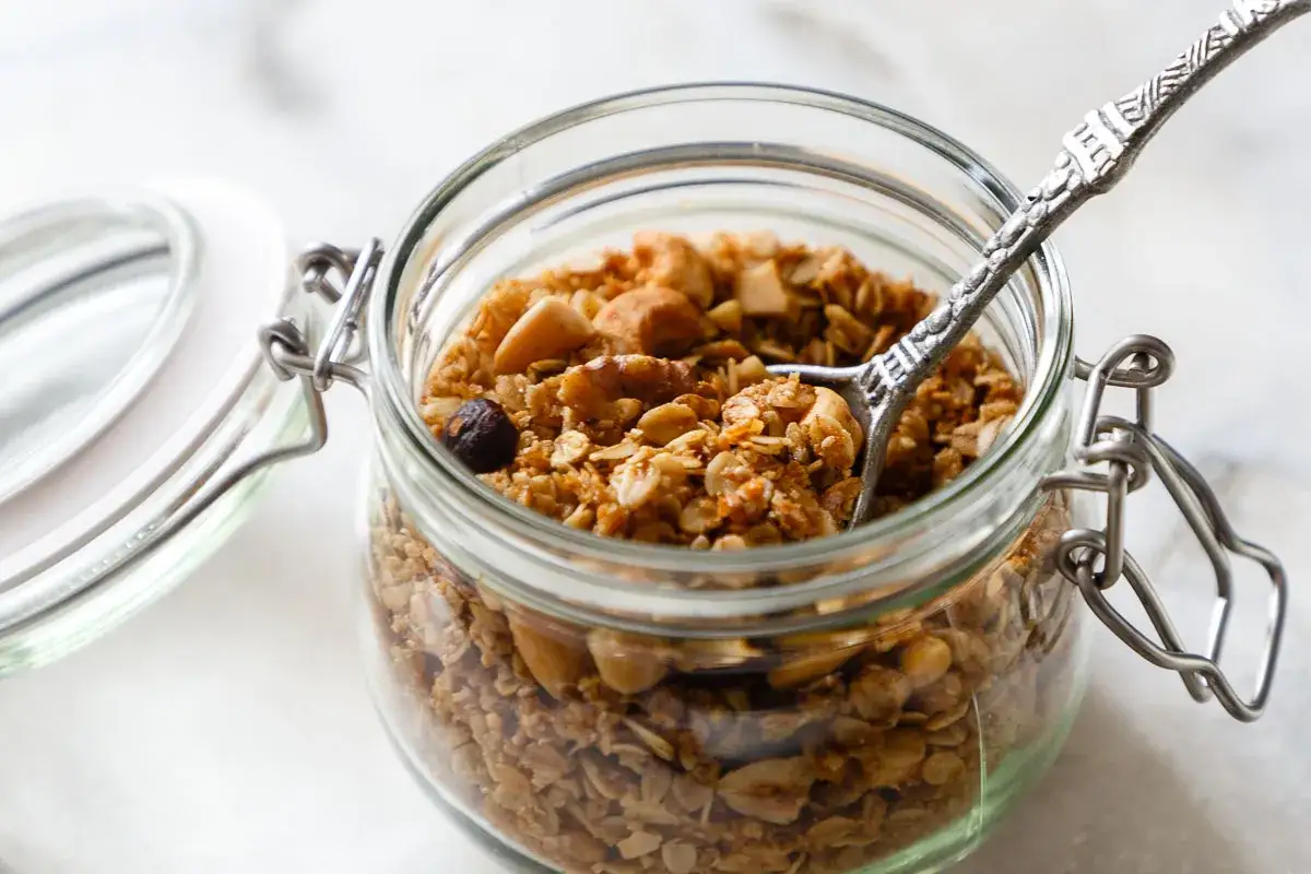 Glas gef&uuml;llt mit selbstgemachtem Granola, perfekt f&uuml;r gesunde Fr&uuml;hst&uuml;cksrezepte. Eine L&ouml;ffelspitze ragt heraus.