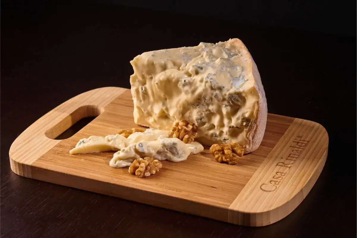 Un pezzo di zola formaggio cremoso con venature blu, servito su un tagliere di bambù con noci.