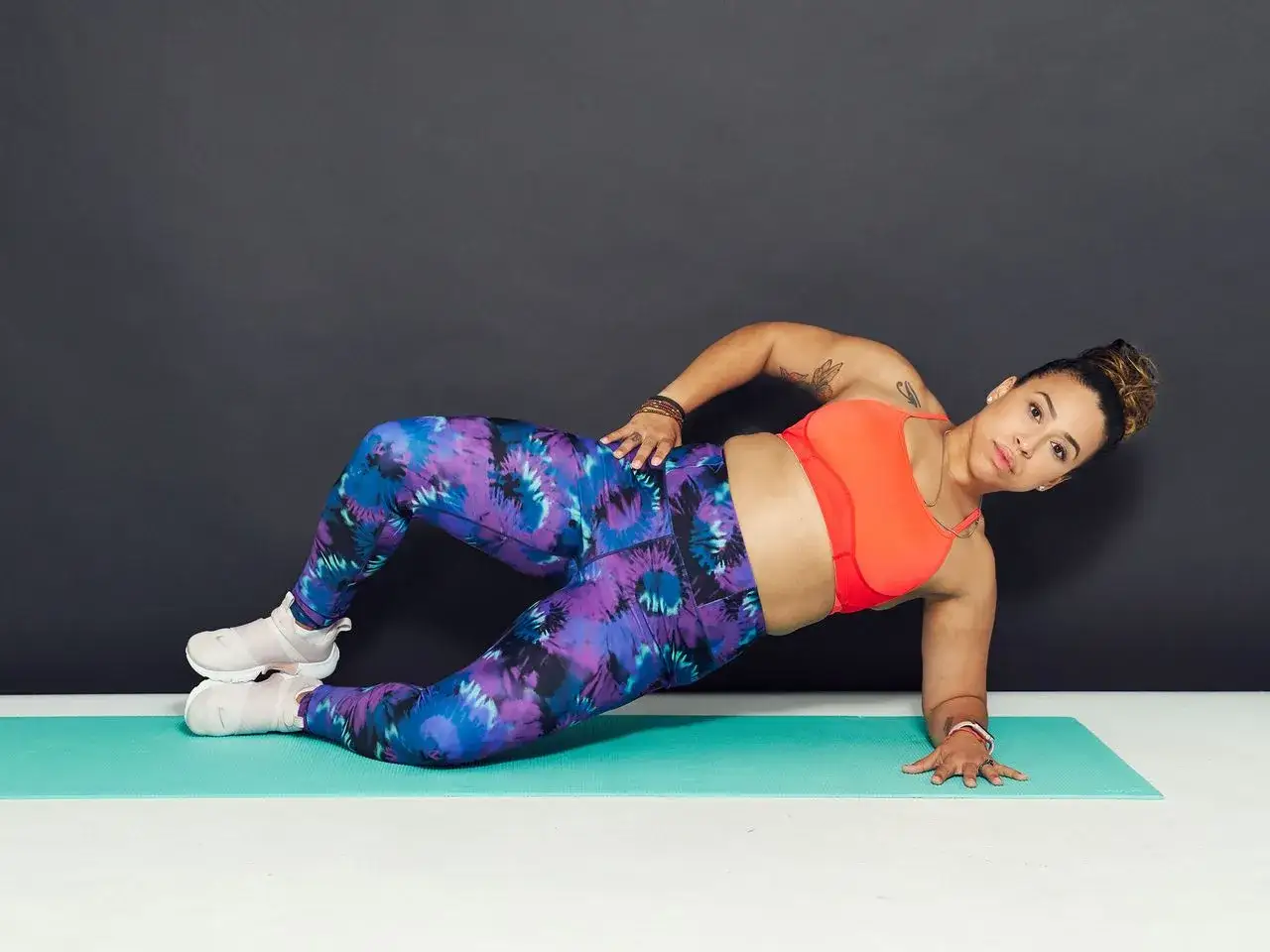 Femme en tenue de sport color&eacute;e, effectuant un exercice de gainage lat&eacute;ral. Ses jambes sont pli&eacute;es, cr&eacute;ant des **fentes** douces, tandis qu'elle soutient son corps sur son avant-bras.