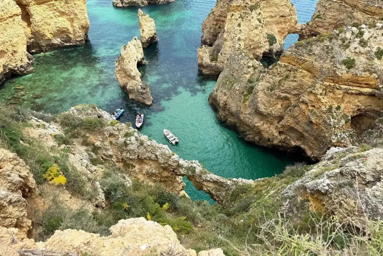 Senderismo Algarve: acantilados dorados, aguas turquesas y barcas explorando cuevas marinas.