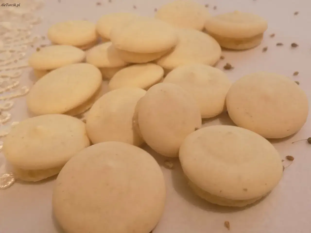 Stosik jasnych ciasteczek, przypominających anyżki, leży na koronkowym obrusie.