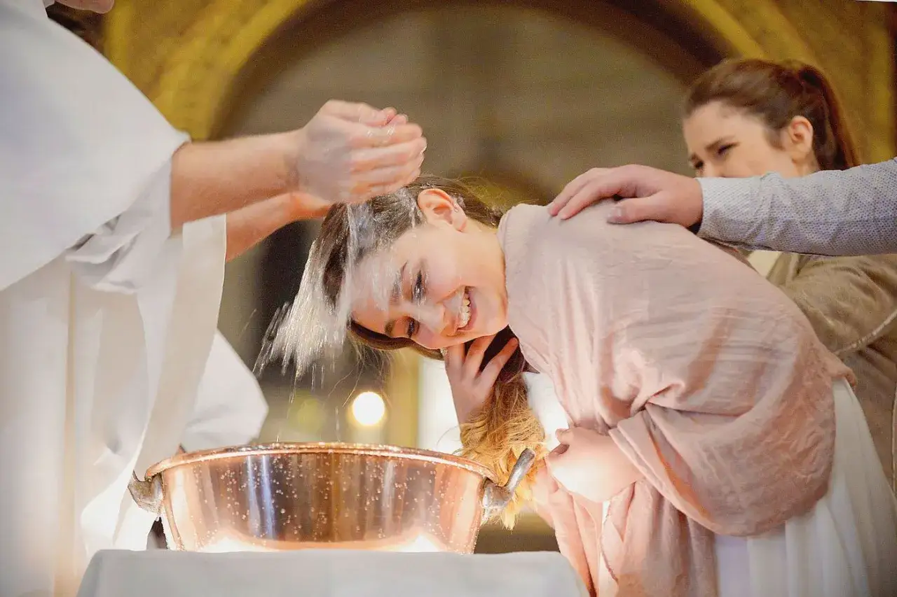 Une jeune fille souriante se fait baptiser &agrave; 16 ans. L'eau b&eacute;nite coule sur sa t&ecirc;te dans un baptist&egrave;re en cuivre.