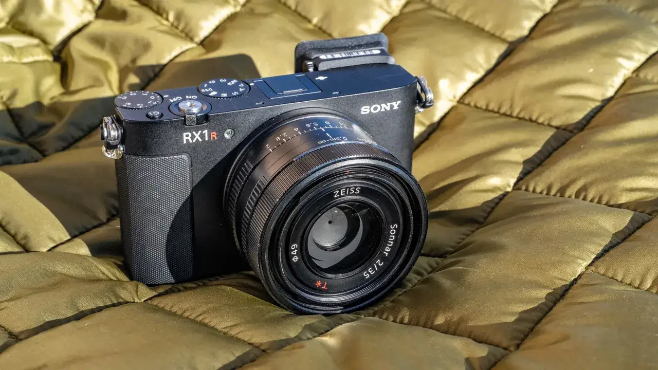 En svart Sony RX1R-kamera med ett Zeiss Sonnar 2/35-objektiv ligger p&aring; ett olivgr&ouml;nt, quiltat tyg.