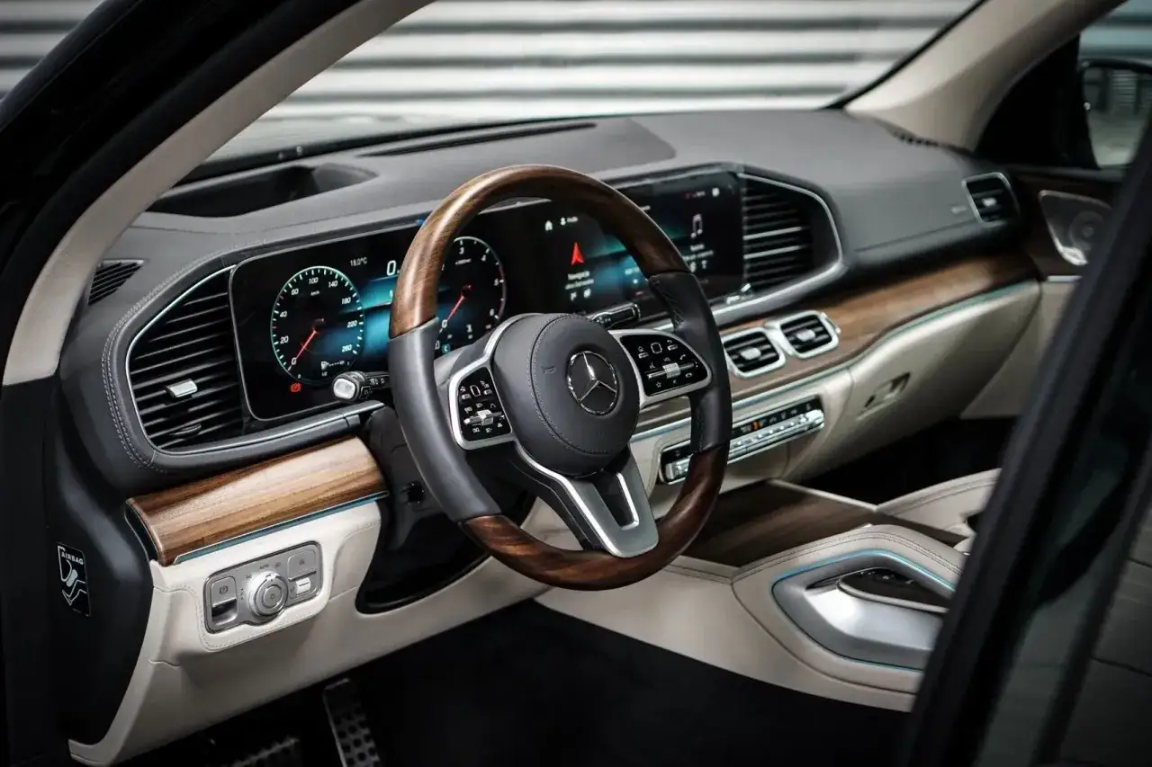 Wnętrze luksusowego **Mercedes GLS 2025** z drewnianymi akcentami, cyfrowymi zegarami i skórzaną kierownicą.