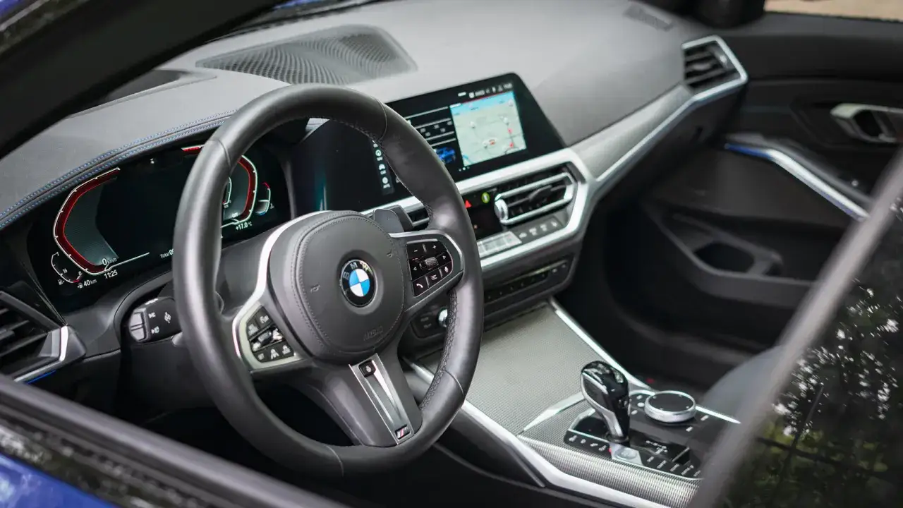 Wnętrze BMW 318i: kierownica, cyfrowe zegary i ekran multimedialny.