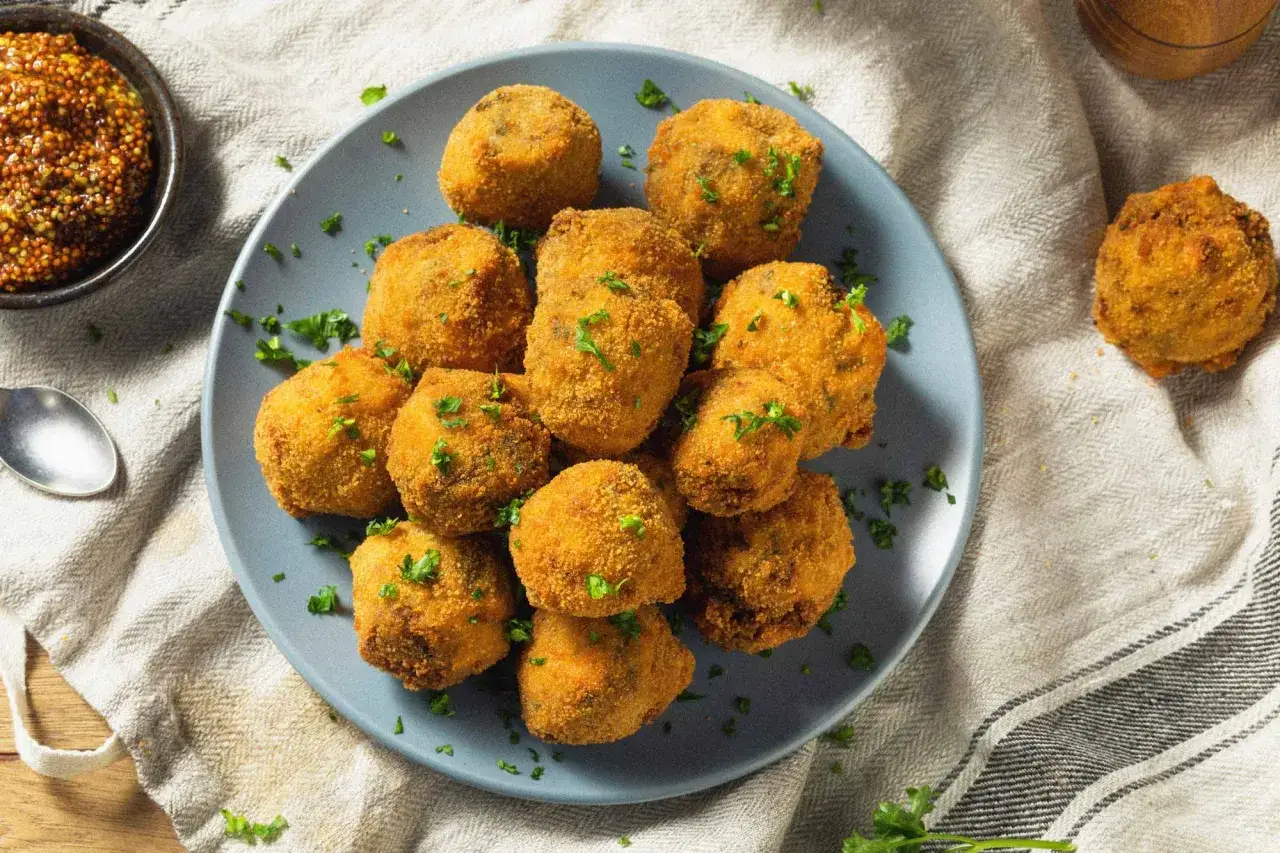 Knusprige Bitterballen auf einem Teller, garniert mit Petersilie. Ein köstliches Bitterballen Rezept zum Nachmachen. Daneben eine Schüssel mit Senf.