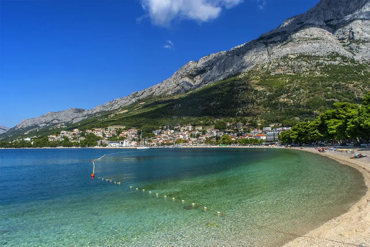 Czysta woda i piaszczysta plaża na Makarskiej Riwierze, z górami w tle.