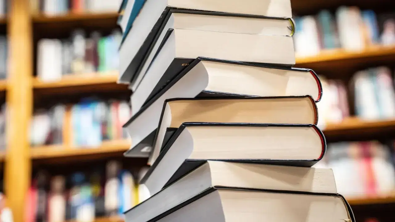 Stapel von B&uuml;chern, die wie ein Sunday Times Bestseller aussehen, stehen vor einem unscharfen B&uuml;cherregal.