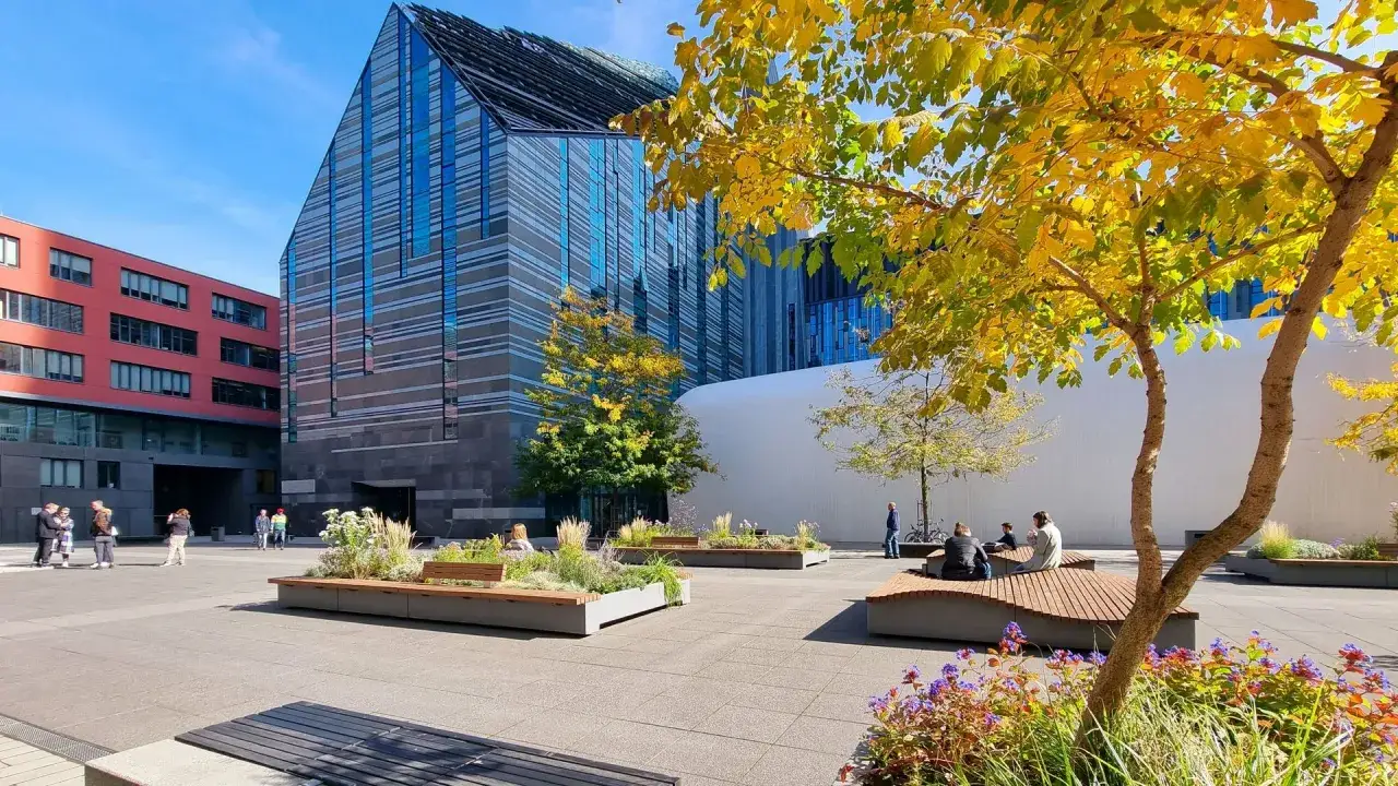Herbstliche Szene auf dem Campus der Universit&auml;t Leipzig. Studierende entspannen sich auf modernen B&auml;nken im Freien, umgeben von bunten B&auml;umen und Blumen.