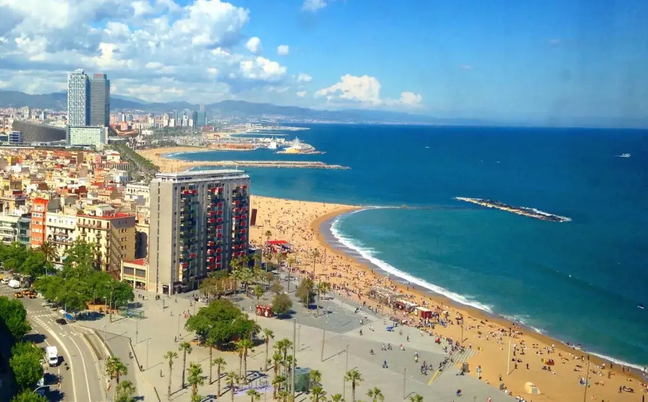 Widok na Barcelonę nad Morzem Śródziemnym. Tłumy ludzi na plaży, budynki i palmy.